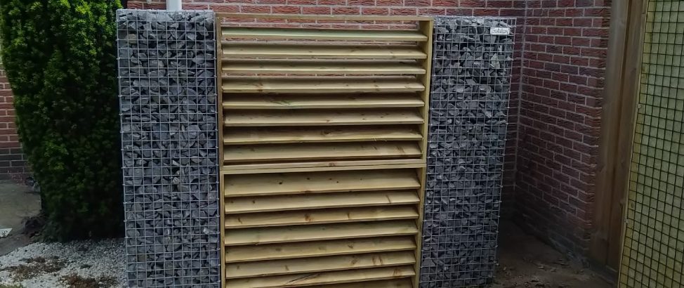 Twee schanskorfzuilen met ertussen een houten deur ter afscheidingswand voor de containers.